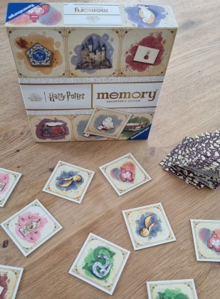 Auf dem Bild sind die Spielebox mit dem Titel und verschiedene aufgedeckte Karten mit Bildmotiven abgebildet (Schnatz, Liebestrank, Berti-Botts-Bohnen, Slytherin-Symbol).