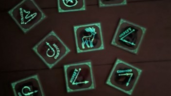 Auf dem Bild sind mehrere Plättchen abgebildet, auf denen unterschiedliche Symbole (Hirsch, Zauberstabbewegungen) durch Phosphorfarbe leuchten.